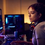 Female Teenage Hacker Sitting In Front Of Computer Screens Bypassing Cyber Security