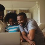 Parents and daughter using laptop in living room